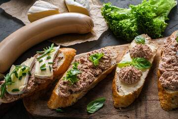 Delicious sandwiches with pate, cheese, greens, spices on cutting board with onion on dark background. Meat food, top view