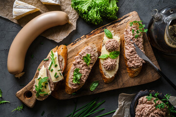 Delicious sandwiches with pate, cheese, greens, spices on cutting board with onion on dark background. Meat food, top view