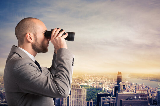 Businessman looks at the city landscape with binoculars