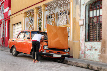 A Cuban man fixing his orange car in the city of Santiago De Cuba 