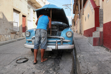 A Cuban man fixing his blue car in the city of Santiago De Cuba 