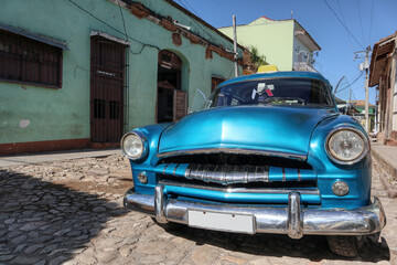 A photo of a light blue old American car using as a Cuban taxi  parked on the street of Trinidad 
