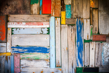 Photo of a well worn wooden wall with multicoloured planks and vignetting added.