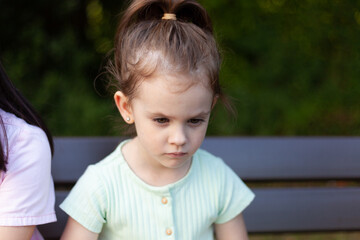 Little girl sitting on a bench in the park and looking at the camera