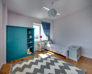 Kid's bedroom with light walls and a parquet with carpet on the floor. There is a bed with colorful...