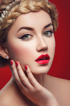 Beautiful young woman with full red lips and braid hairstyle touching face. Beauty shot over red background.