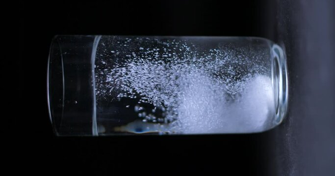 Aspirin falling into a glass of water on black background, vertical slow motion 4K Pro Res