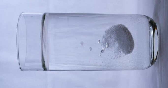 Aspirin falling into a glass of water on black background, vertical slow motion 4K Pro Res