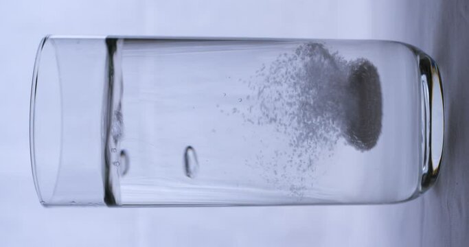 Aspirin falling into a glass of water on black background, vertical slow motion 4K Pro Res