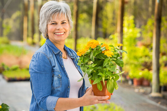 Beautiful mature woman working in a greenhouse holding flowers on her hands