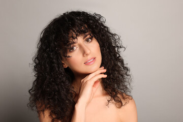 Fototapeta premium Beautiful young woman with long curly hair on light grey background