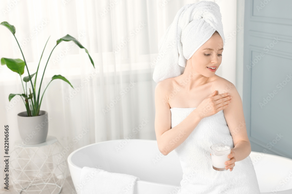 Poster beautiful young woman applying body cream onto shoulder in bathroom