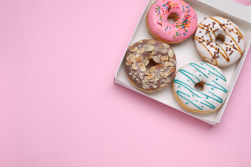 Box with different tasty glazed donuts on pink background, top view. Space for text