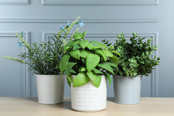 Many different artificial plants in flower pots on wooden table near grey wall