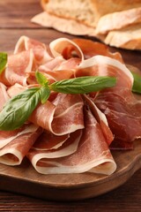 Slices of tasty cured ham and basil on wooden board, closeup