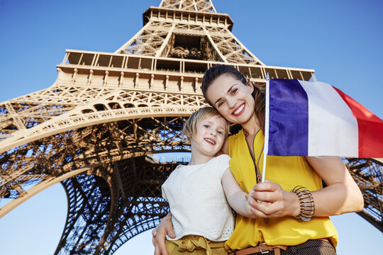 Portrait of smiling mother and child tourists showing flag in the front of Eiffel tower in Paris, France
