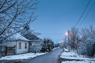 Selective blur on an empty road and street in the village of Bavaniste, in Vojvodina, Banat, Serbia, in the countryside, covered in snow, during a cold freezing night dusk of winter.