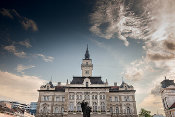 Trg Slobode Square with the city hall, or Gradska Kuca, and the Svetozar Miletic statue created in 1935 by Ivan mestrovic in novi sad, second biggest city of Serbia, with people passing by. - obrazy, fototapety, plakaty