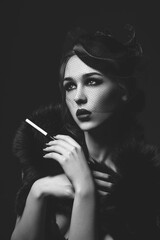 Beautiful young woman with smoky eyes and full red lips holding cigarette holder. Vintage head piece. Retro styling. Studio beauty shot. Copy space. Monochrome.