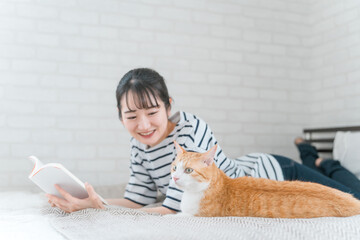 家のベッドルームでペットの猫と遊ぶアジア人女性(読書・スキンシップ)
 - obrazy, fototapety, plakaty