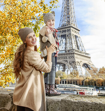 Autumn getaways in Paris with family. Portrait of smiling mother and child travellers on embankment near Eiffel tower in Paris, France handwaving