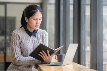 Beautiful woman drinking coffee and reading book on couch, spending free spare time at home.