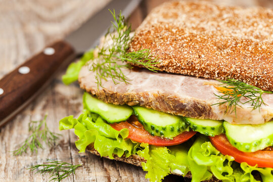Close-up of tasty rye bread sandwiches with roast meat and vegetables, on wooden background