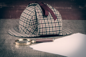 Deerstalker or Sherlock Hat and magnifying glass on Old Wooden table.