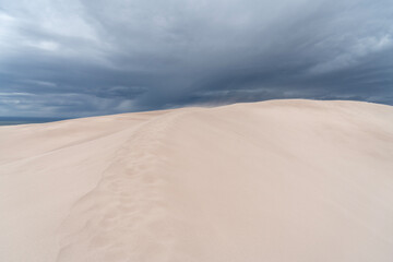 Sand dune with footprints on a path going towards a  dark sky