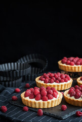 Delicious raspberry mini tarts (tartlets) with whipped cream on dark background