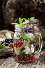 Detox drink with fresh berries, mint and ice in glass jars on wooden background