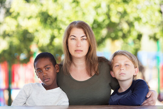 Serious mother sitting in between adopted child and son at table in park