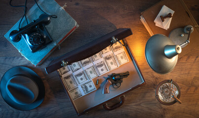 Vintage desktop in the dark with a gun, a briefcase and a lot of dollar packs, top view