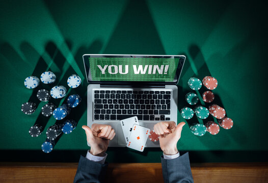 Man thumbs up playing online poker with laptop on a green table with chips all around, top view
