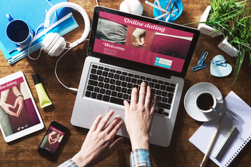 Online dating website on a laptop display, hardwood desktop and stationery on background