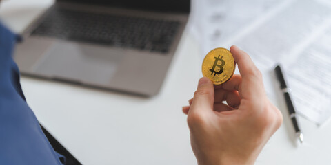 Investing on Bitcoin Cryptocurrency concept. Businessman hands hold gold Bitcoin Cryptocurrency with computer laptop and financial paperwork on white desk to analyze for trading and investing. Banner. - 622126328