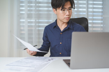 Business casual. Asian young Businessman using computer laptop with long casual business shirt when working at workplace. Business man holds business contract agreement document for approved project. - 622126339
