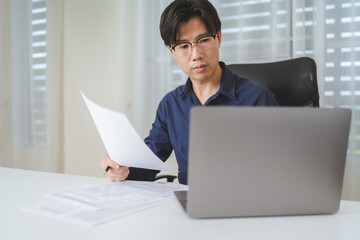 Asian businessman holds business contract agreement for check and manage business contract document with laptop. Investor analyzing business document paperwork for decide to investment on business - 622126346