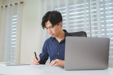 Asian trader or businessman using tablet and computer laptop for planning for financial investing as Bitcoin Cryptocurrency. Male investor wearing glasses, trading on online stock market platform. - 622126364