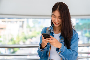 Young asian woman walking and using smartphone on the street - Powered by Adobe