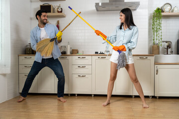 Young happy couple having fun while doing cleaning kitchen together