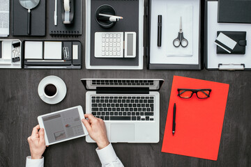 Corporate businessman working at office desk, he is networking with a digital tablet, flat lay