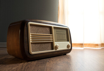 Vintage radio next to a window with curtain on hardwood floor.