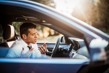 Businessman driving a car and arguing on his smart phone while on a commute to work
