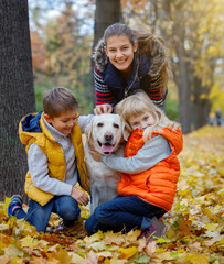 Cute kids and dog Labrador retriever posing in autumn park. Yellow and orange leaves around.