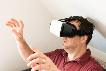 Caucasian man resting on comfortable sofa wearing VR headset glasses and making gestures