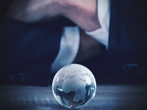 Businessman with world glass sphere with continents on the table
