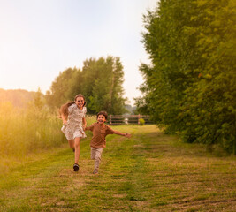 Obraz premium Little boy and girl run in the meadow at sunset