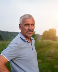 Portrait of a senior man standing in a field at sunset.