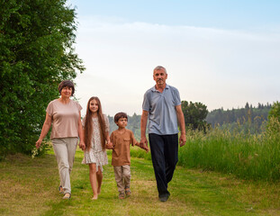 Happy family walks in the park on a summer day. Grandfather, grandmother and grandchildren.